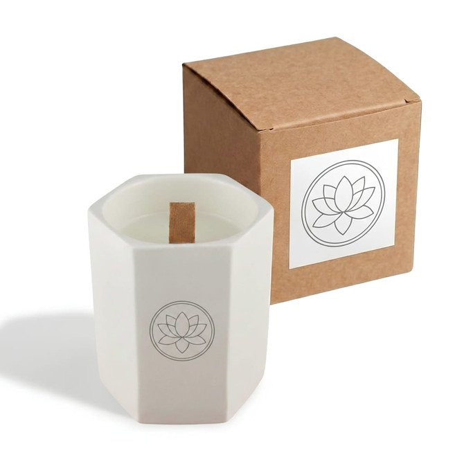 A hexagon-shaped white ceramic candle with a wooden wick, next to a brown cardboard box. It features a logo.