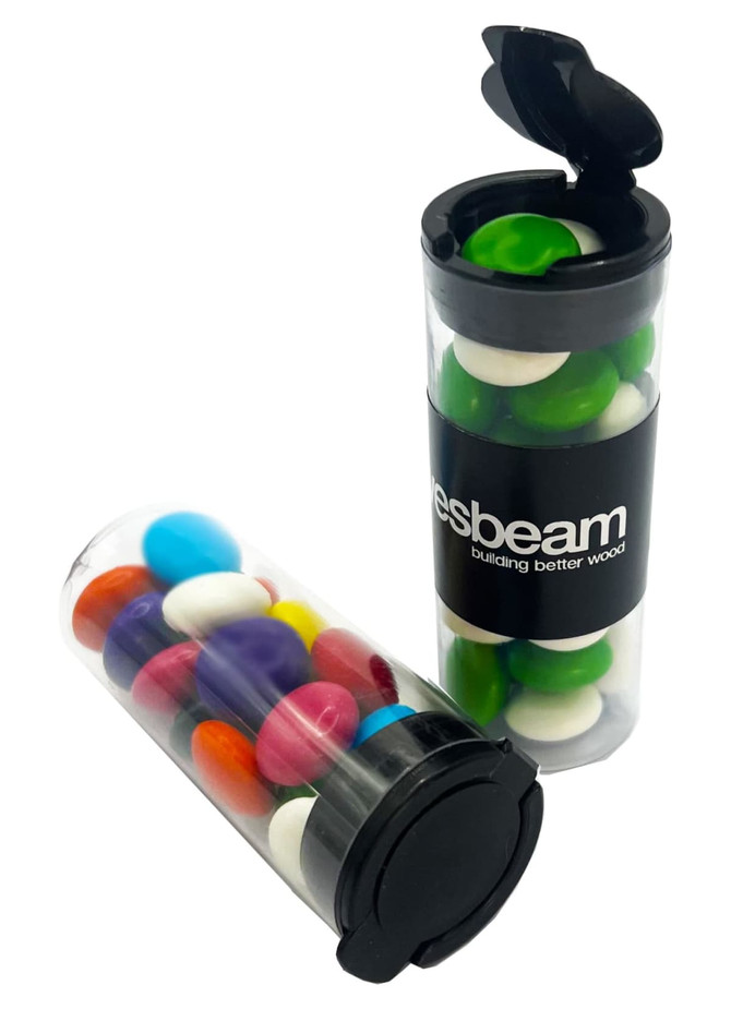 A clear flip lid tube containing colourful choc beans in various shades, with a black branding band.
