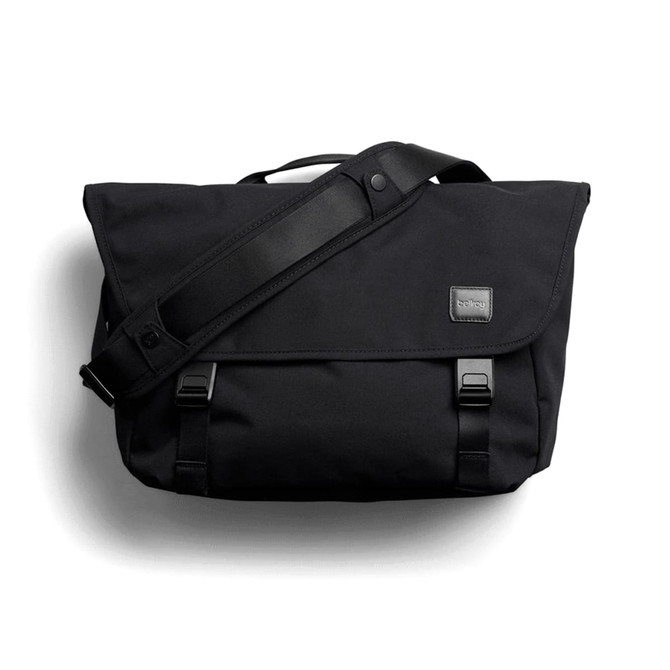 A black messenger bag with a flap, adjustable shoulder strap, and branding label. It features buckle closures and a sleek design.