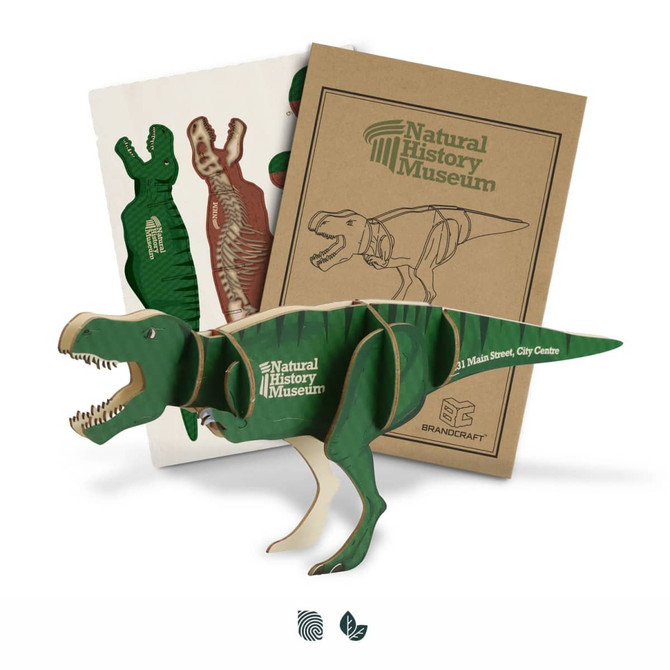 A green wooden Tyrannosaurus Rex model next to instructional sheets, featuring a logo on the packaging.