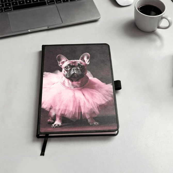 A notebook with a black cover featuring a pink tutu-wearing dog on the front. It includes a logo.
