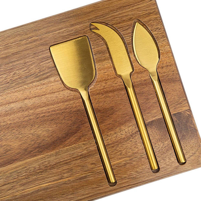 A wooden cheeseboard featuring three gold-coloured knives shaped for cutting and serving cheese.