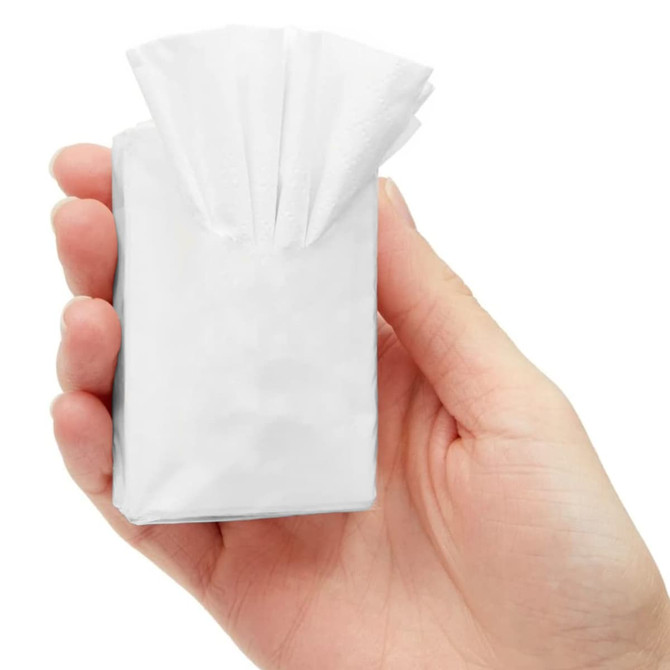 A hand holding a small, white packet of tissues with multiple tissues protruding from the top.