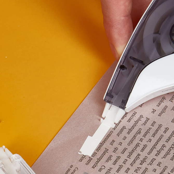 A correction tape dispenser with a black and white design, being used on a sheet of paper.
