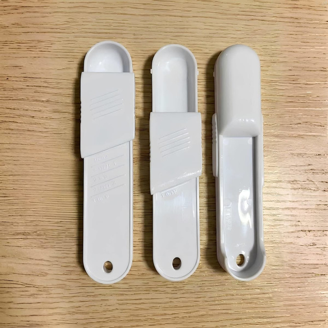 Three white measuring scoops arranged on a wooden surface, featuring different designs and shapes.