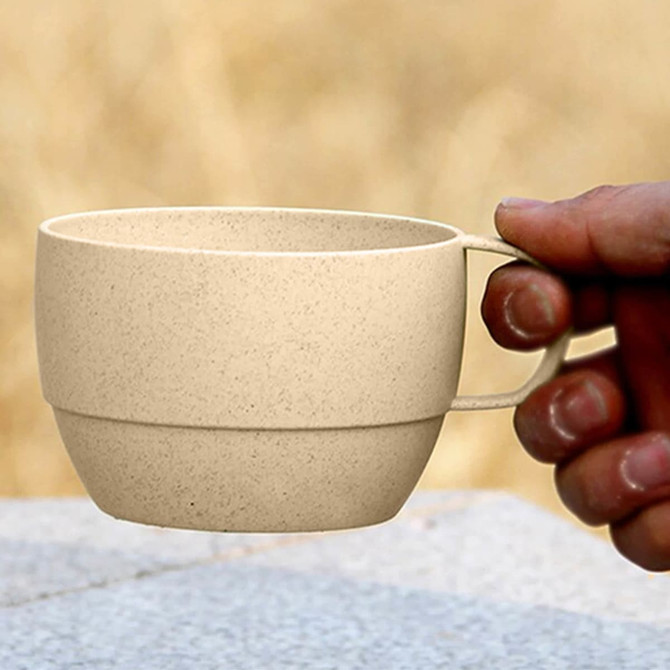 A reusable coffee cup made of wheat straw, featuring a beige colour and a handle. Includes a logo.