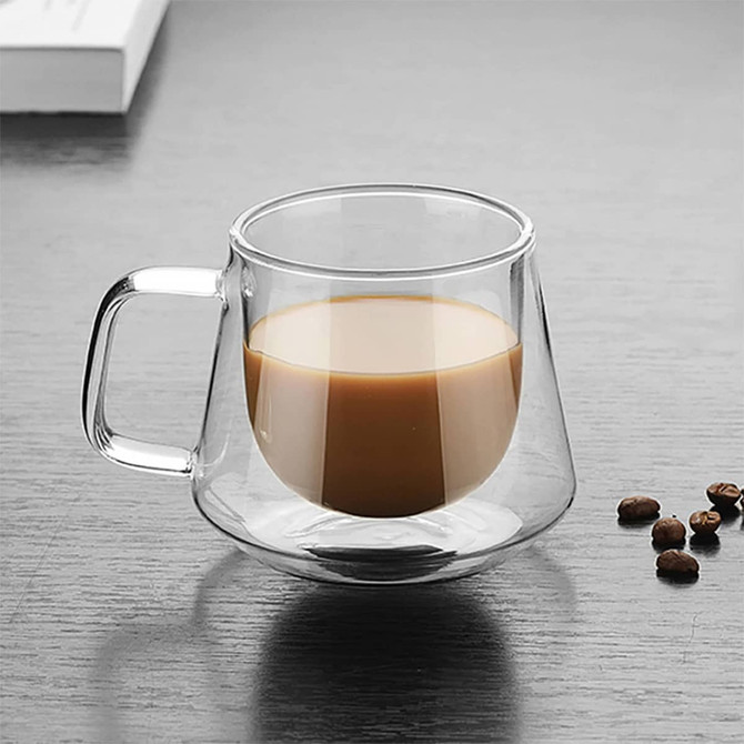 A glass coffee cup with a unique design, featuring a mix of clear and tinted glass. It includes a handle and sits on a wooden surface.