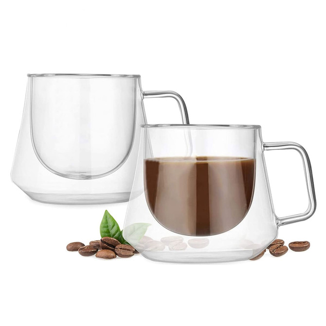 A pair of clear, double-walled glass coffee cups with a sleek design, accompanied by coffee beans and leaves.