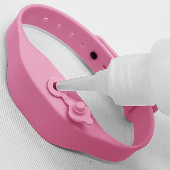 A pink wristband hand sanitiser dispenser with a nozzle dispensing sanitiser through a small opening.
