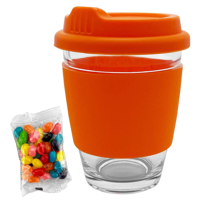 A clear glass coffee cup with an orange silicone sleeve and lid, accompanied by a pack of colourful jelly beans.