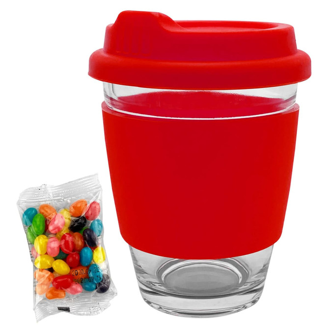A glass coffee cup with a red silicone lid and sleeve, accompanied by a pack of colourful jelly beans.