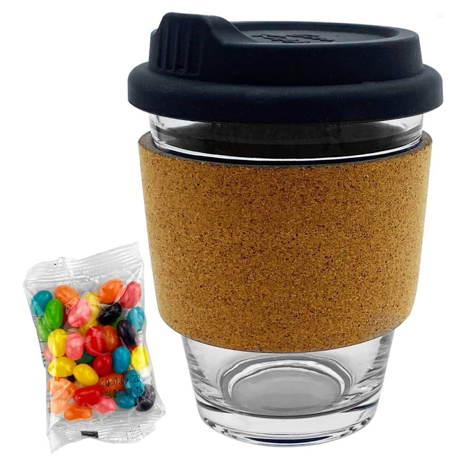 A glass coffee cup with a black lid and cork band, accompanied by a packet of colourful jelly beans.