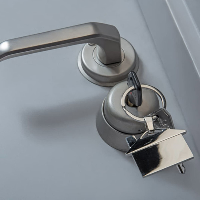 A silver house-shaped key ring attached to a silver door handle, set against a grey background.