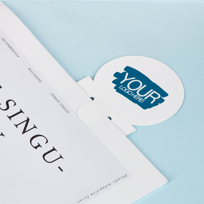 A bookmark ruler with a circular top featuring a logo, placed on a blue background with partially visible pages.