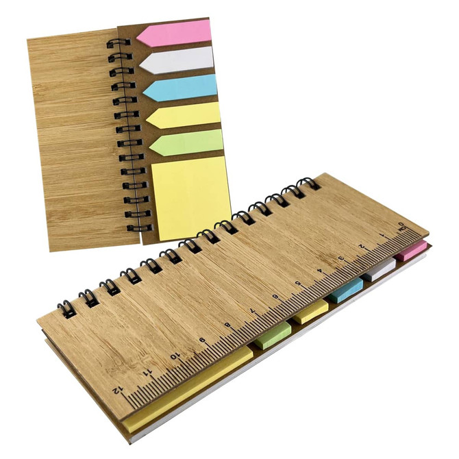 A bamboo sticky note holder with yellow, pink, and blue sticky notes and a ruler along one edge. It features a spiral binding.