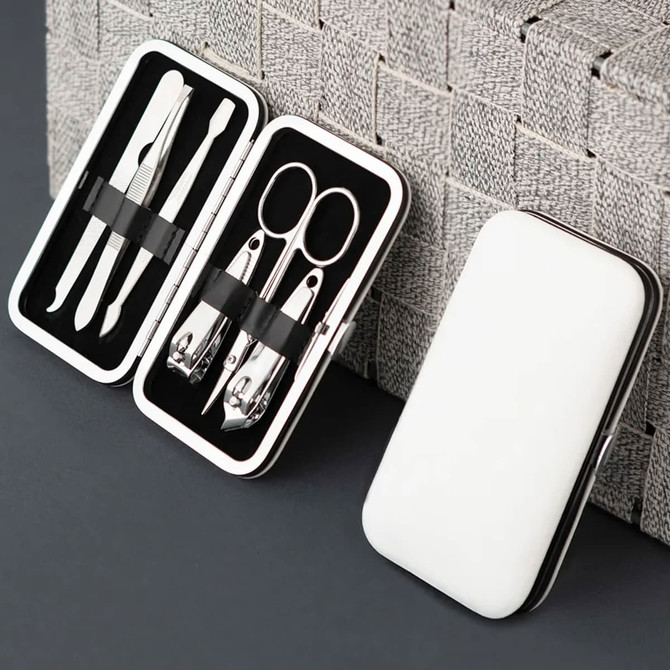 A sleek white manicure set case containing stainless steel tools like scissors, clippers, and tweezers.