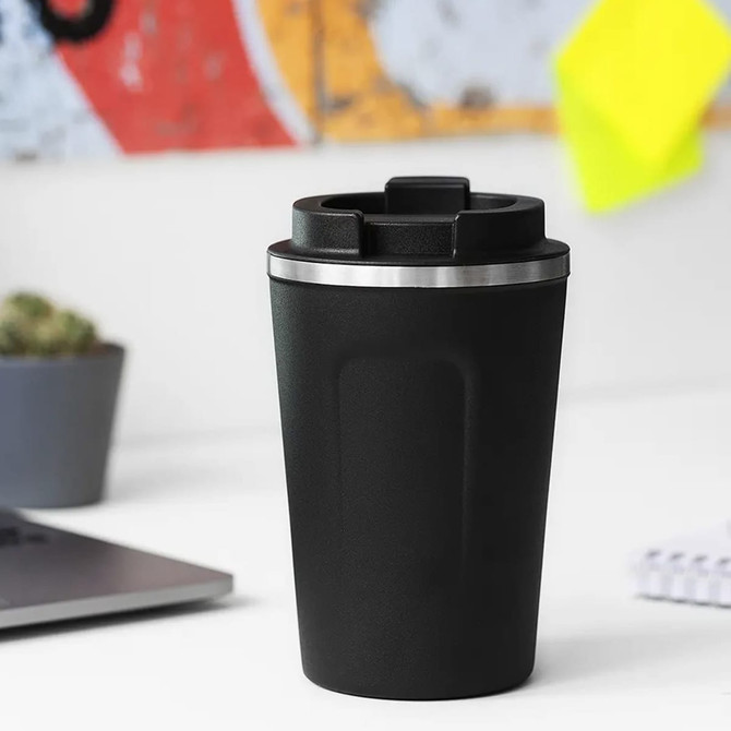 A reusable coffee cup in sleek black with a stainless steel lid, featuring a logo and set against a minimalist workspace.