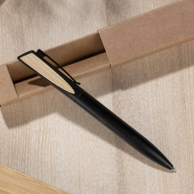 A black metal pen with a wooden accent, resting on a light wooden surface near a cardboard box.