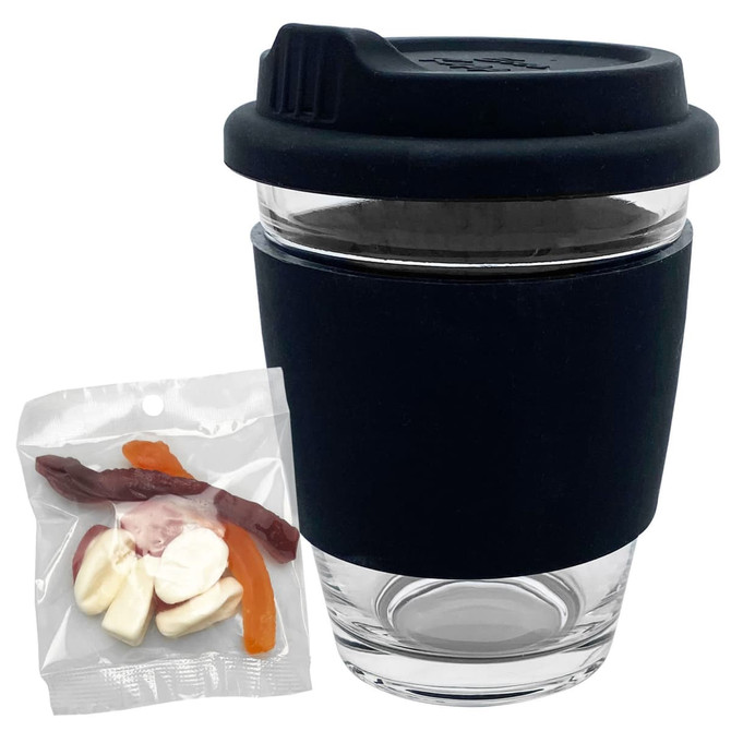 A reusable clear glass coffee cup with a black silicone sleeve beside a packet of jelly sweets.