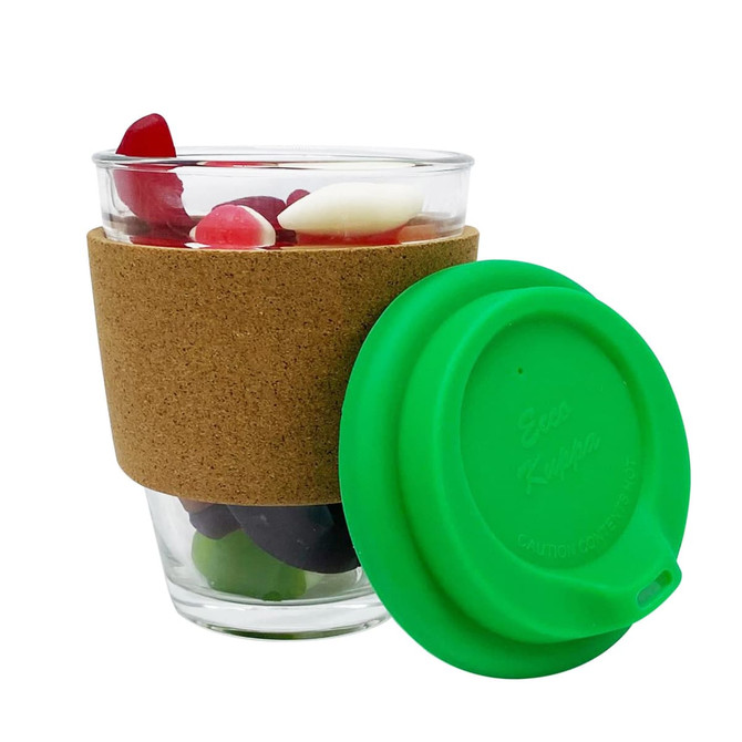 A glass coffee cup filled with mixed lollies, featuring a cork band and a green silicone lid.