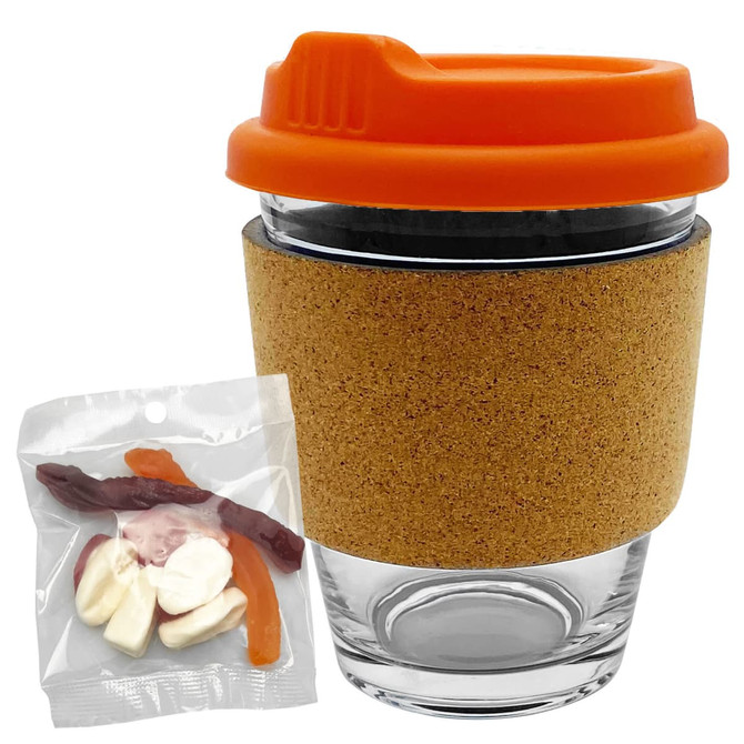 A glass coffee cup with an orange lid and cork band, accompanied by a bag of mixed lollies in various colours.