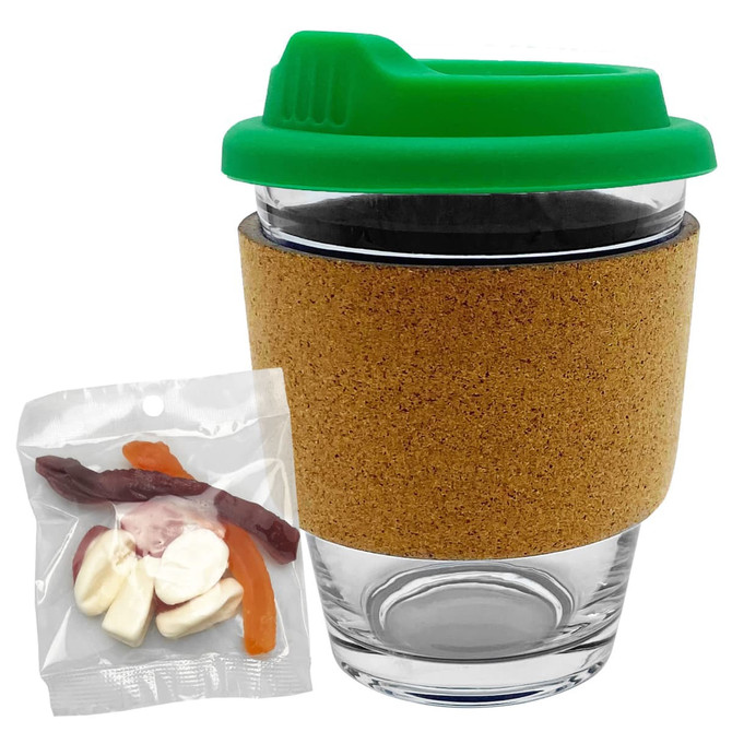 A clear glass coffee cup with a green lid and cork band, accompanied by a pack of mixed lollies in assorted colours.