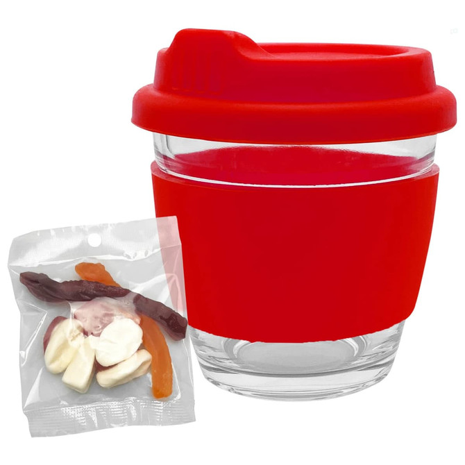 A transparent glass coffee cup with a red silicone lid and sleeve, alongside a pack of mixed jelly lollies.