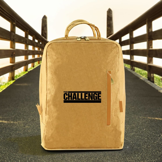 A kraft paper laptop backpack in a tan colour, featuring a logo on the front, set against an outdoor background.