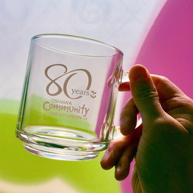 A glass mug with a transparent design and a handle, featuring a logo and decorative elements.