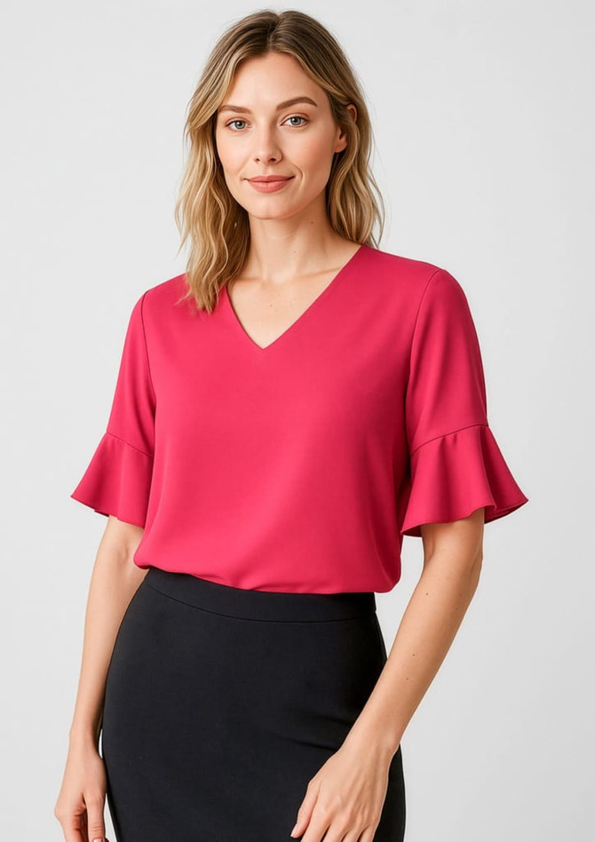 A woman wearing a pink fluted sleeve blouse with a V-neckline, paired with a black skirt. The image features a brand logo.