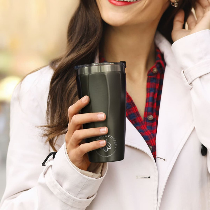A drink bottle in dark green, held by a person wearing a light jacket, with a logo visible on the tumbler.
