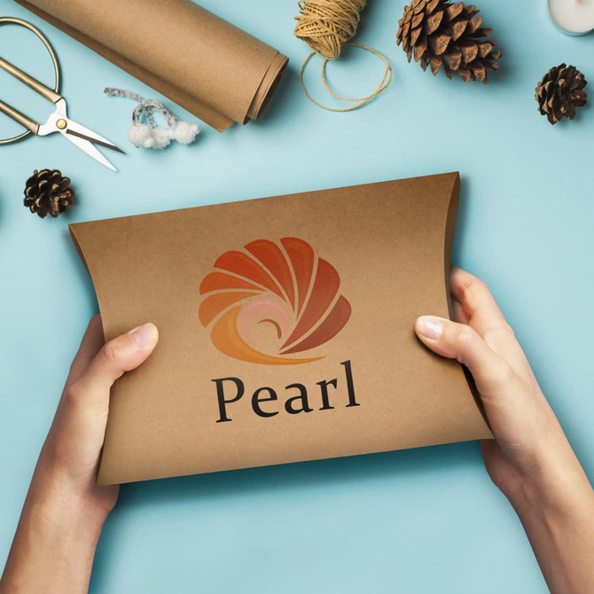 A person holding a large, brown pillow box with a logo on it, surrounded by crafting materials and pinecones.