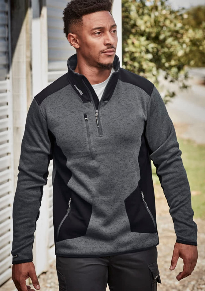 A man wears a grey and black Unisex Streetworx Reinforced Knit 1/2 Zip Pullover, featuring a zippered pocket and side pockets.