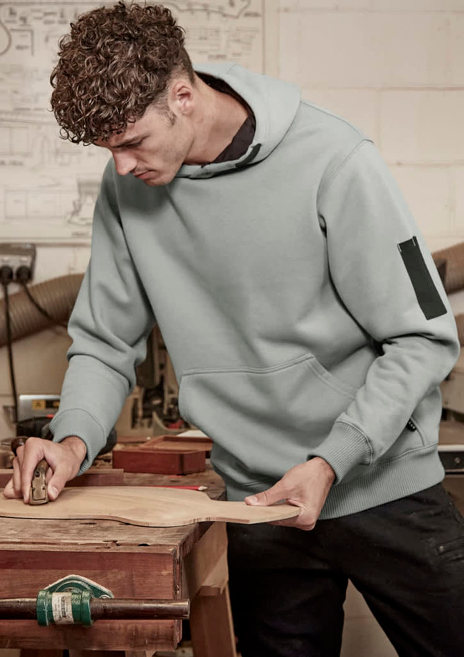 A light blue unisex multi-pocket hoodie worn by a man working in a workshop, featuring a logo on the sleeve.