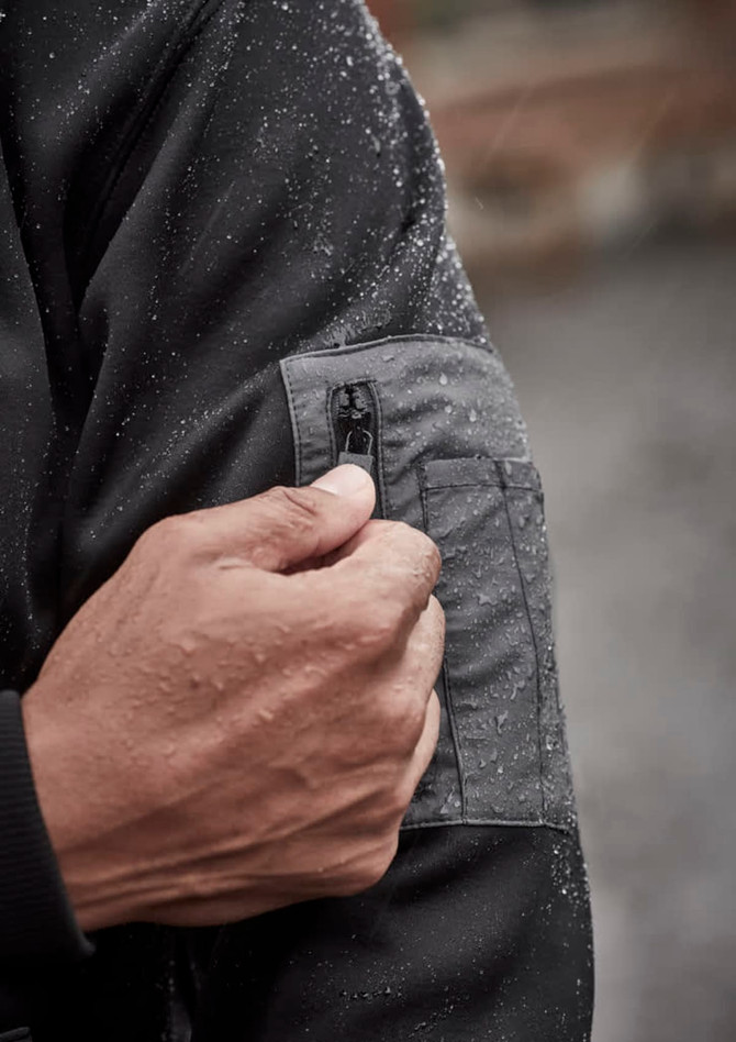 A close-up of a hand adjusting the zipper on a black water-resistant hoodie, showing droplets of water on the fabric.