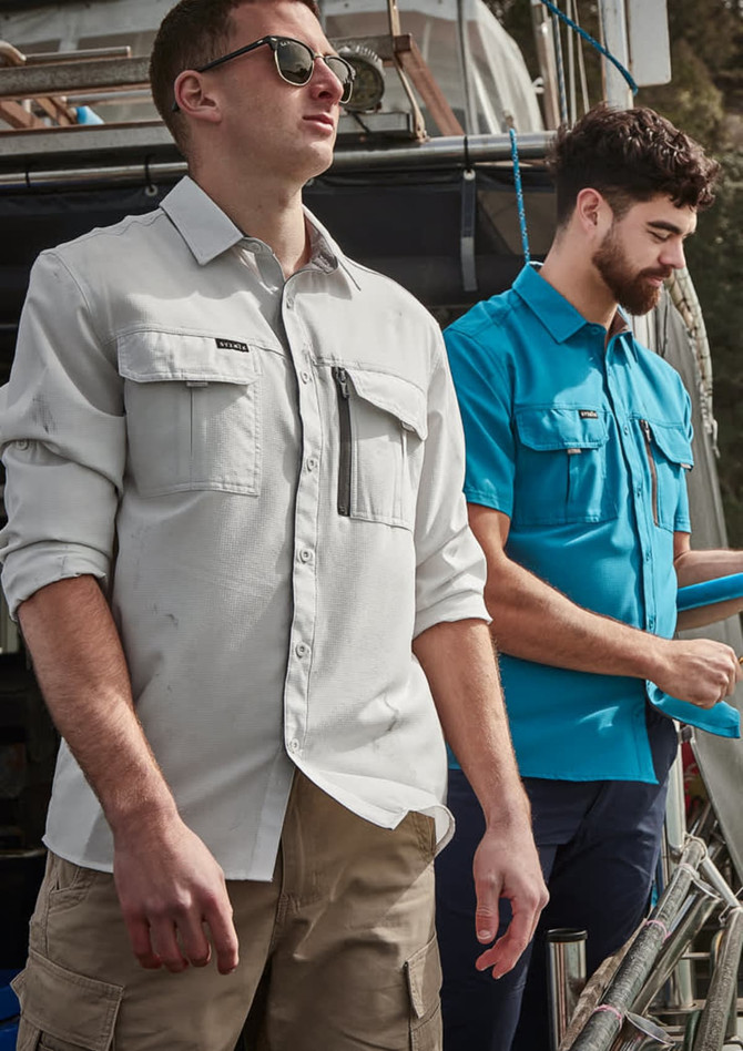 Men wearing long sleeve button-up shirts in light grey and blue, with cargo shorts, standing on a boat.