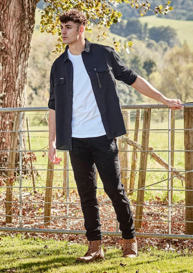 A long sleeve black button-up shirt worn over a white t-shirt, paired with black pants and boots, outdoors.