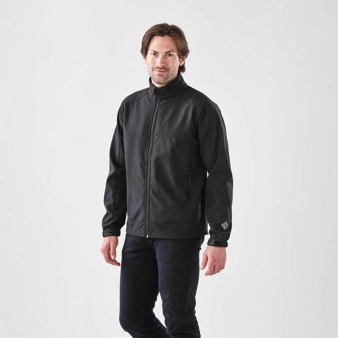 A man wearing a black Men's Cirrus Bonded Jacket, featuring a zip front and side pockets, with a logo on the sleeve.