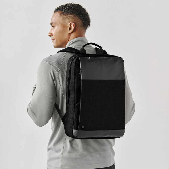 A man wearing a grey and black laptop bag on his back, featuring a logo and a minimalist design.