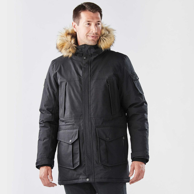 A man wearing a black parka jacket with a fur-lined hood, featuring multiple pockets and a stylish design.