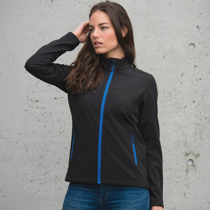 A black women's softshell jacket with blue zip accents and two side pockets, displayed on a model against a concrete background.