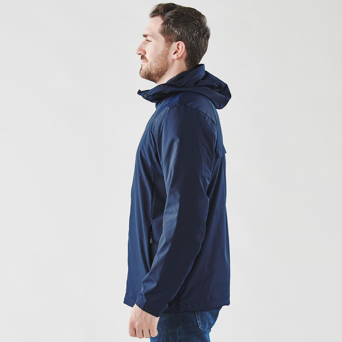 A man is wearing a navy blue wind jacket featuring a hood and a logo, shown from the side.