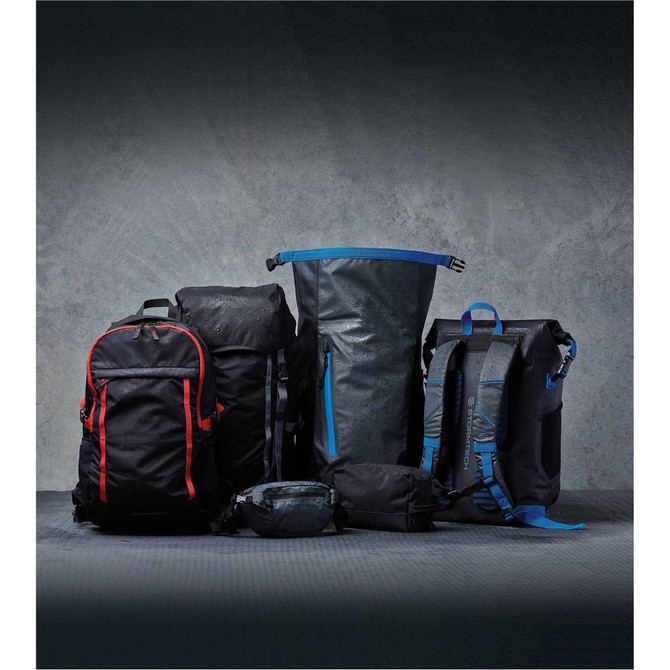 A collection of bags including a black hip pack, black backpacks with red accents, and a large blue-detailed black bag.