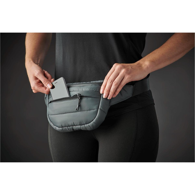 A quilted grey waist bag with a front zipper pocket and a phone being placed inside.