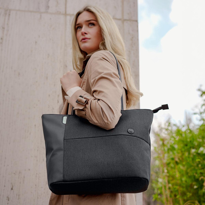 A woman carries a stylish black and grey tote bag with a logo, set against an outdoor background.