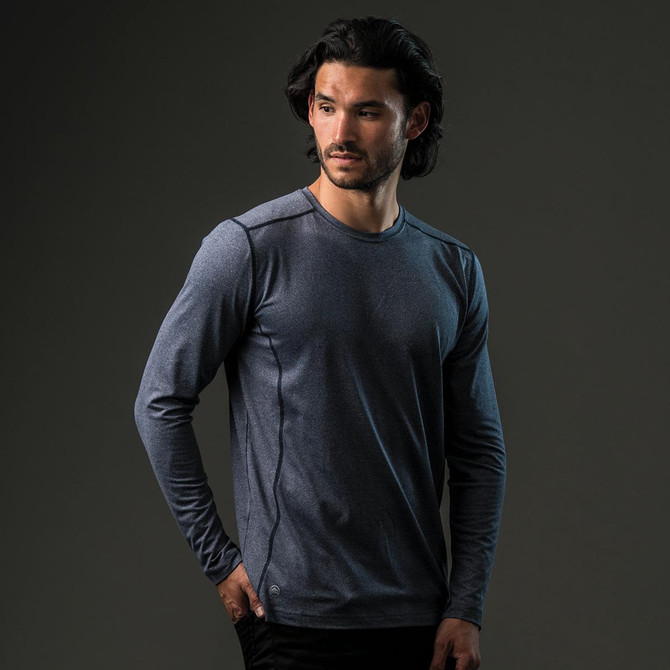 A man models a long-sleeve, navy blue T-shirt featuring a logo. The shirt has a slim fit and subtle detailing.