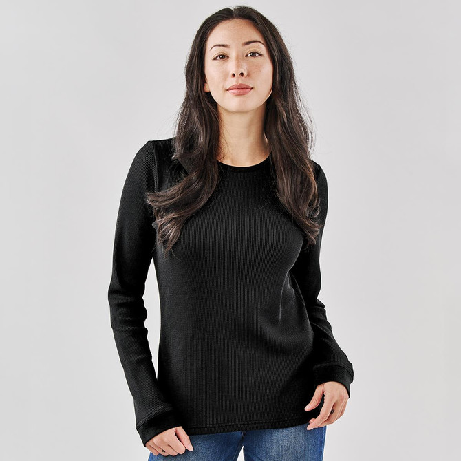 A black crew neck shirt featuring long sleeves, worn by a model. The shirt has a subtle ribbed texture and a logo.