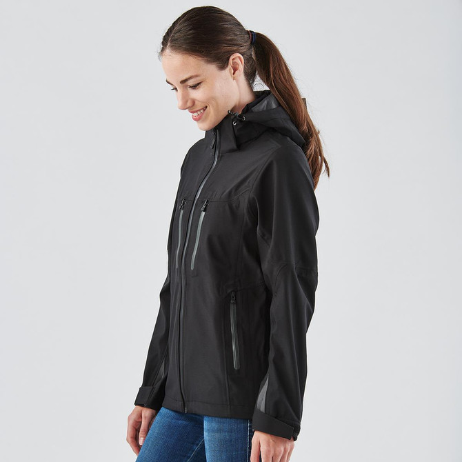 A woman wearing a black softshell jacket with a hood, featuring zippered pockets and a fitted design.