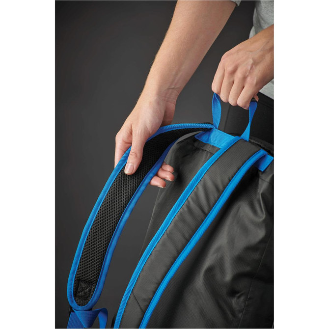 A person's hand holds the padded blue strap of a black backpack, showcasing its design and features.