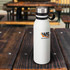 A drink bottle in white with a stainless steel lid and a black handle, featuring a logo.